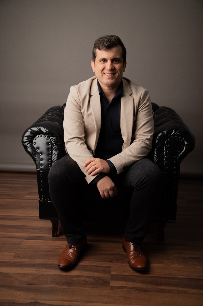 Dr. Rodrigo Siqueira, blazer bege, sentado em poltrona, sorrindo em estúdio profissional